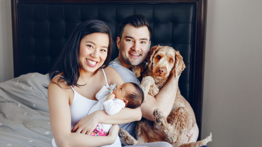 family smiling while holding baby and dog
